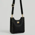 Angled view of the structured black pebbled leather messenger bag featuring gold side studs and an adjustable buckle strap