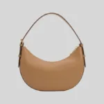 Front profile of a tan half-moon commuter bag featuring gold-tone hardware, top zip, and an adjustable strap.