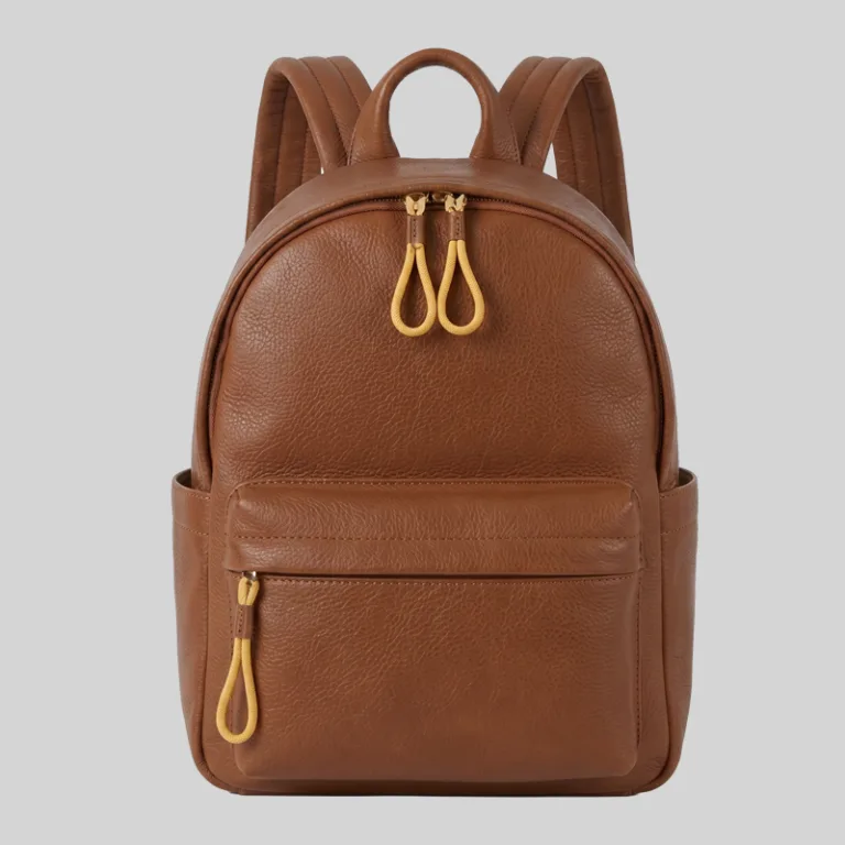 Front view of structured brown top-grain cowhide commuter backpack featuring distinct yellow cord zipper pulls and side pockets for wholesale.