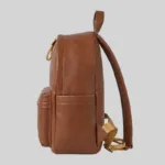 Side profile of brown top-grain cowhide backpack showing side slip pocket depth, structural gusset, and strap attachment points.