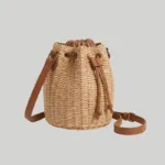 Woven straw bucket bag detailing antique-tone metal eyelets and faux-leather trim