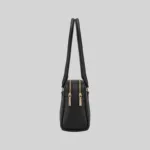 Side profile of the structured black East-West shoulder bag highlighting dual top zippers and gold-tone hardware.