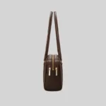 Side profile of the structured dark brown East-West shoulder bag highlighting dual top zippers and gold-tone hardware.