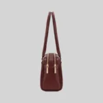 Side profile of the structured burgundy East-West shoulder bag highlighting dual top zippers and gold-tone hardware.
