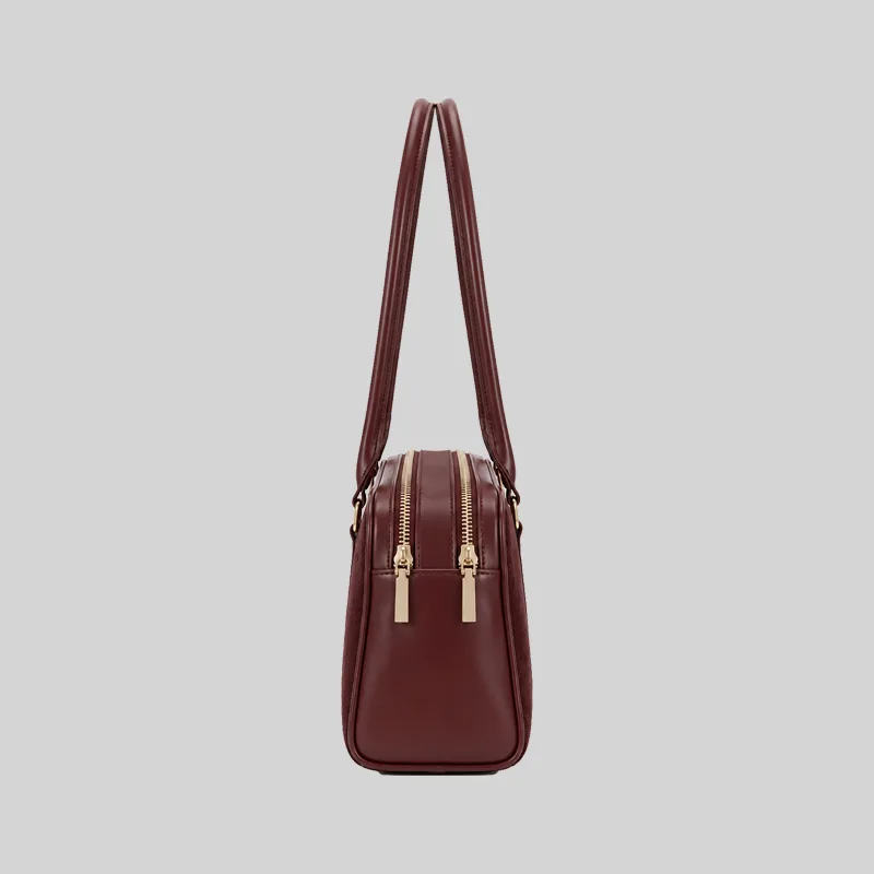 Side profile of the structured burgundy East-West shoulder bag highlighting dual top zippers and gold-tone hardware.