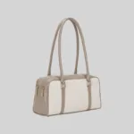 Side view of the structured commuter shoulder bag showing the double zip closure and gold-tone hardware, beige