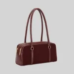 Side view of the structured commuter shoulder bag showing the double zip closure and gold-tone hardware, burgundy
